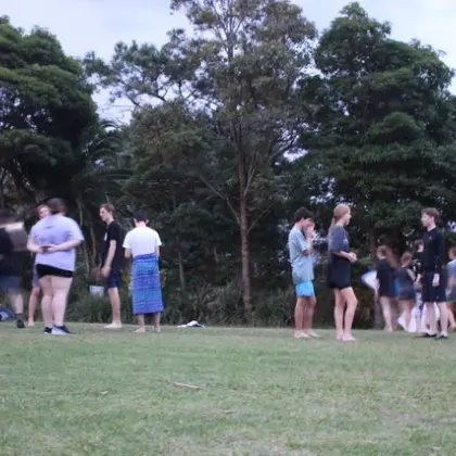 Groups of teenagers standing and chatting on a grassy field among tall trees