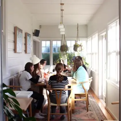 Young people sitting around a long table on a sunny enclosed verandah
