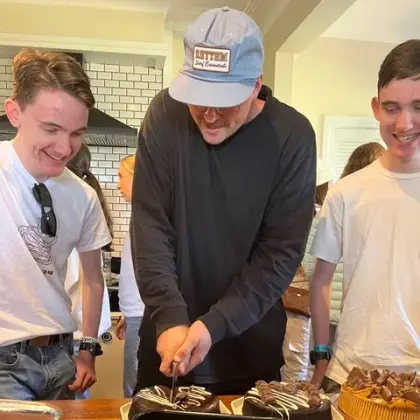 A youth leader cutting chocolate cakes while smiling teenagers look on
