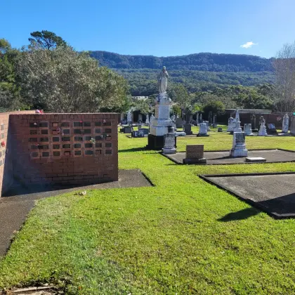 Brick columbarium wall with memorial plaques beside the historic graveyard, with the escarpment behind