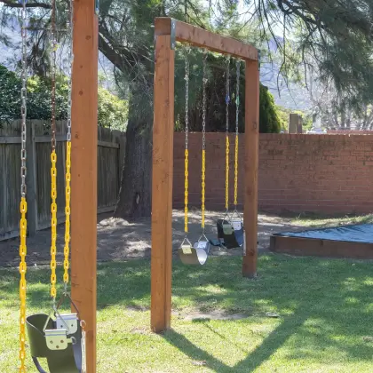 Baby swings on a wooden frame beside a covered sandpit in the church playground