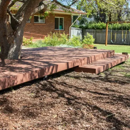 Timber deck built around a tree trunk on a mulched area, with swings in the background