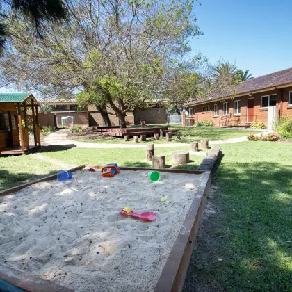 Sandpit with toys in the church playground, with a timber cubby house and the brick ministry centre behind