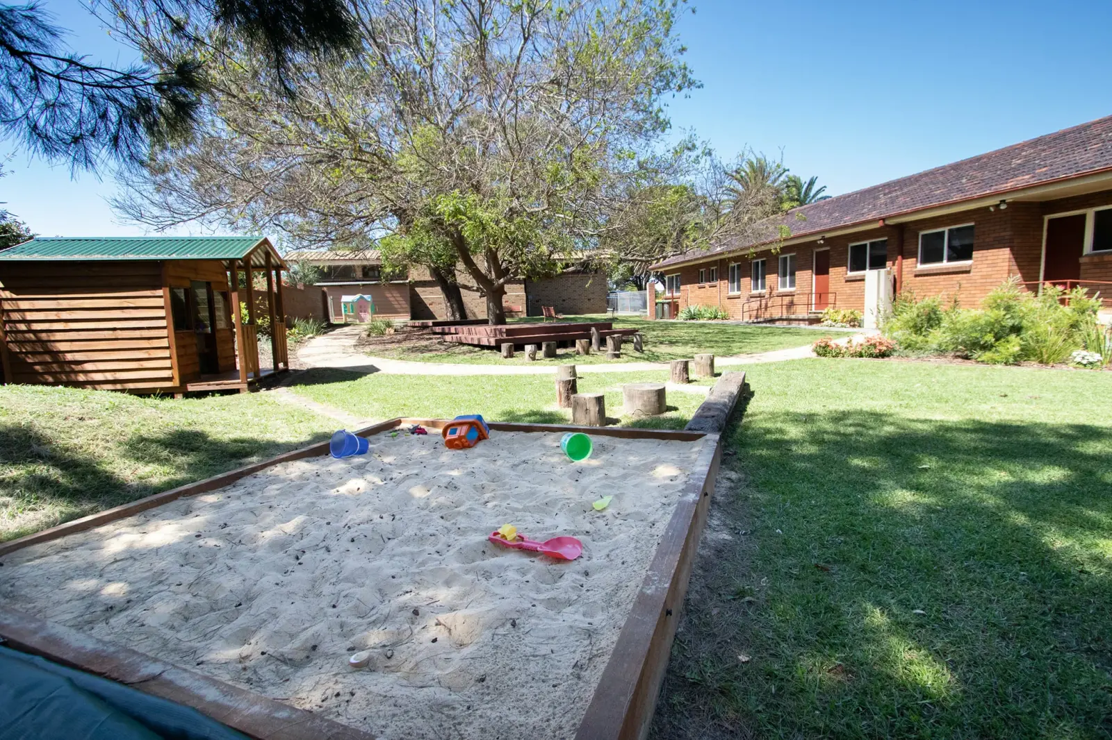 Sandpit with toys in the church playground, with a timber cubby house and the brick ministry centre behind