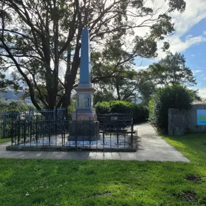 Memorial obelisk inside an iron fence beside the path into the church grounds, with a Bulli Anglican Church sign