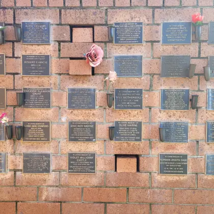 Rows of bronze memorial plaques and flower vases on the brick columbarium wall