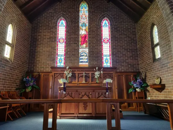 Inside Bulli Anglican Church, with three stained glass windows above the timber communion table